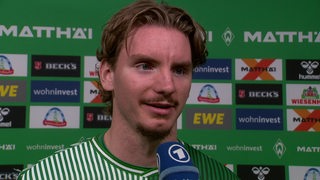 Werder-Stürmer Nick Woltemade nach dem Spiel vor einer Werbewand beim Interview.