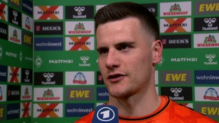 Werder-Torwart Michael Zetterer steht nach dem Spiel vor einer Werbewand beim Interview.