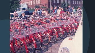 Viele Menschen stehen um mehrere rote Fahrräder herum.