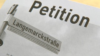 Auf einem Blattpapier steht "Petition" und dadrunter ist ein Foto von dem Straßennamenschild der "Langemarckstraße" zu sehen.